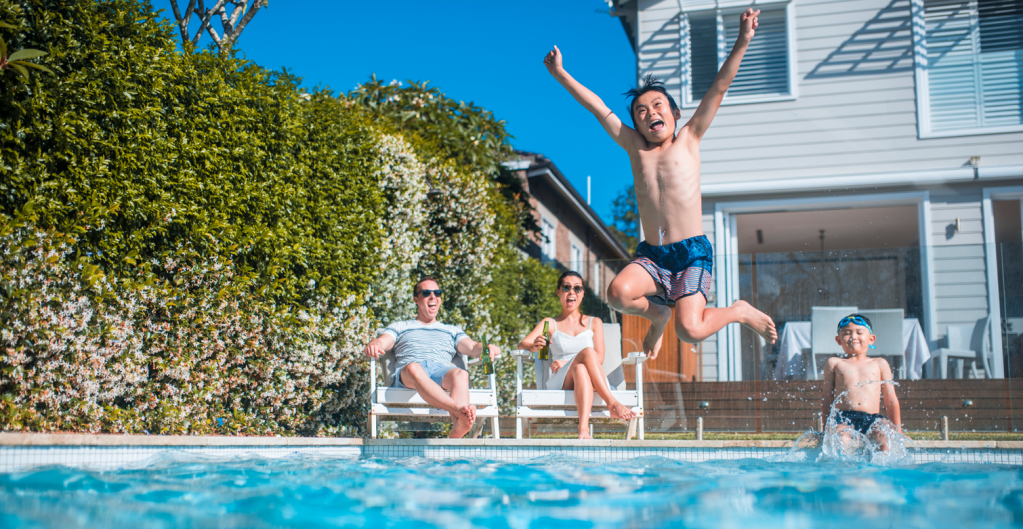 Family laughing by the pool as little boy jumps in.