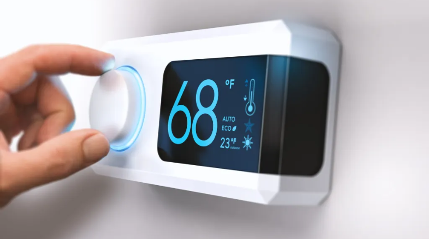 Hand turning a home thermostat knob to set temperature on energy saving mode.