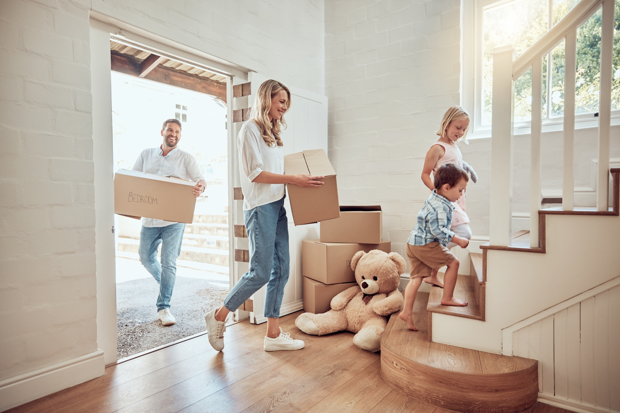 Happy parents carrying boxes up staircase with little kids moving into their new home.