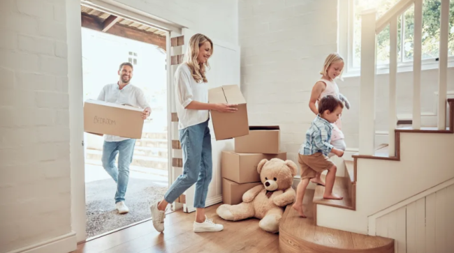 Parents carrying boxes up staircase with kids moving into their new home.