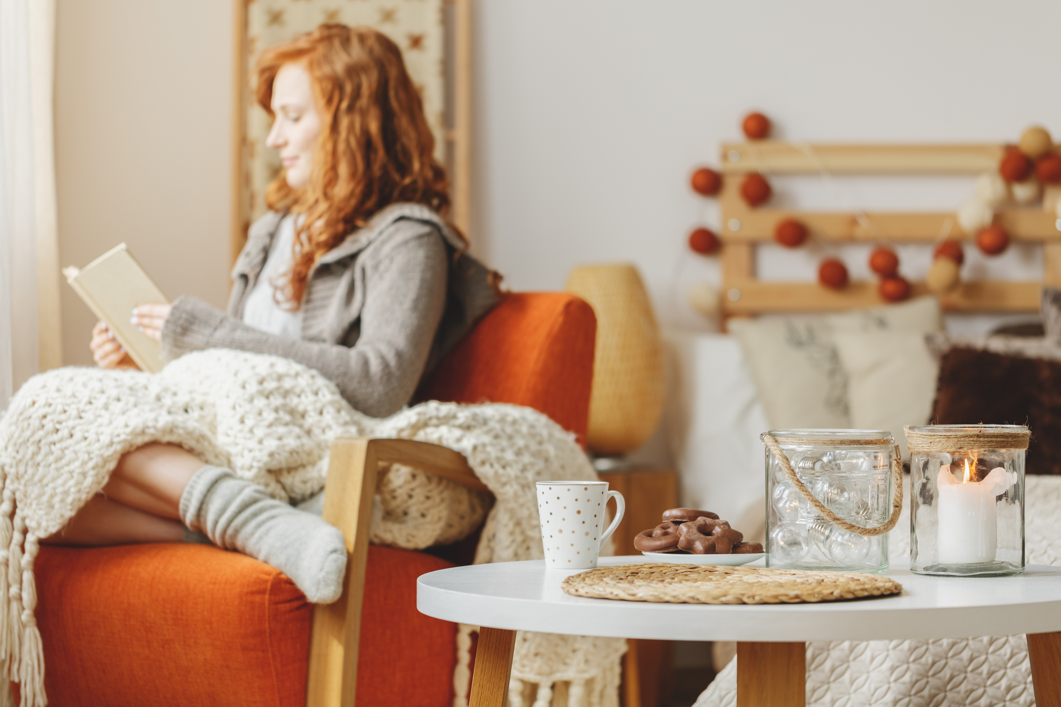 Small table with gingerbread and a tea along with a candle and a young lady reading a book in the background