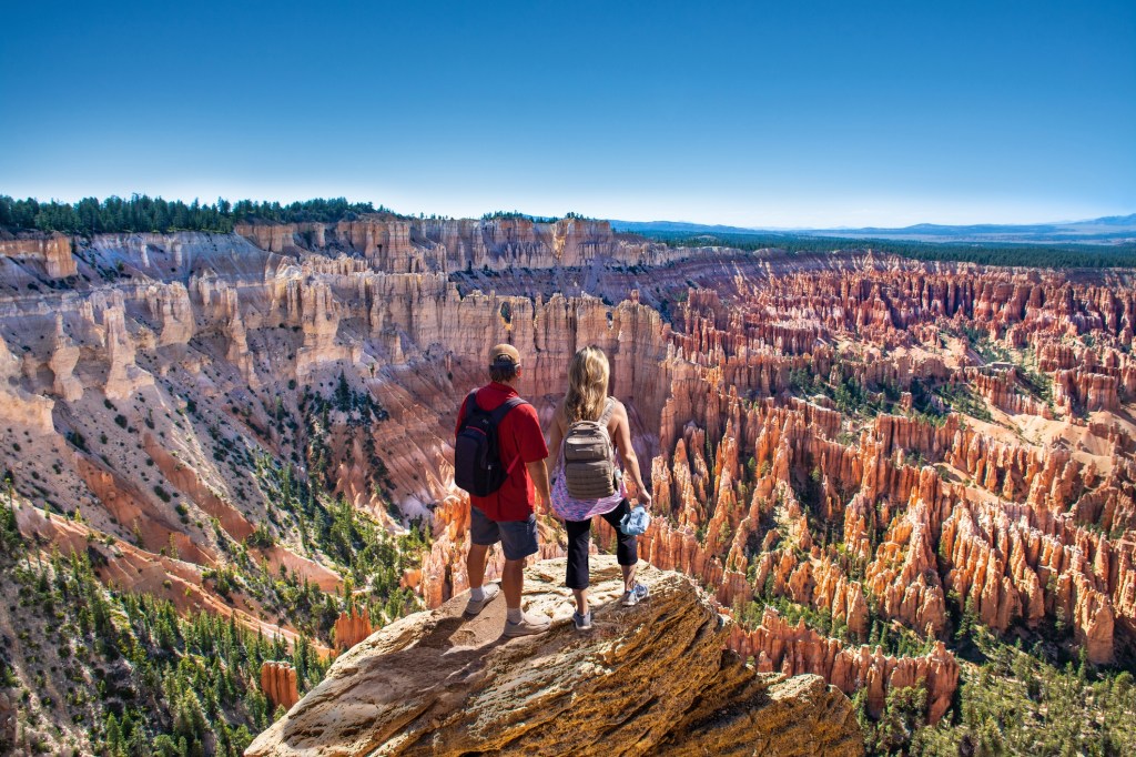 People relaxing on summer vacation hiking trip. Couple looking at beautiful mountain view. Friends standing on the top of the mountain. Inspiration Point, Bryce Canyon National Park, Utah, USA