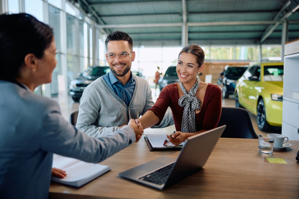 Happy couple shaking hands with saleswoman after buying new car in a showroom.