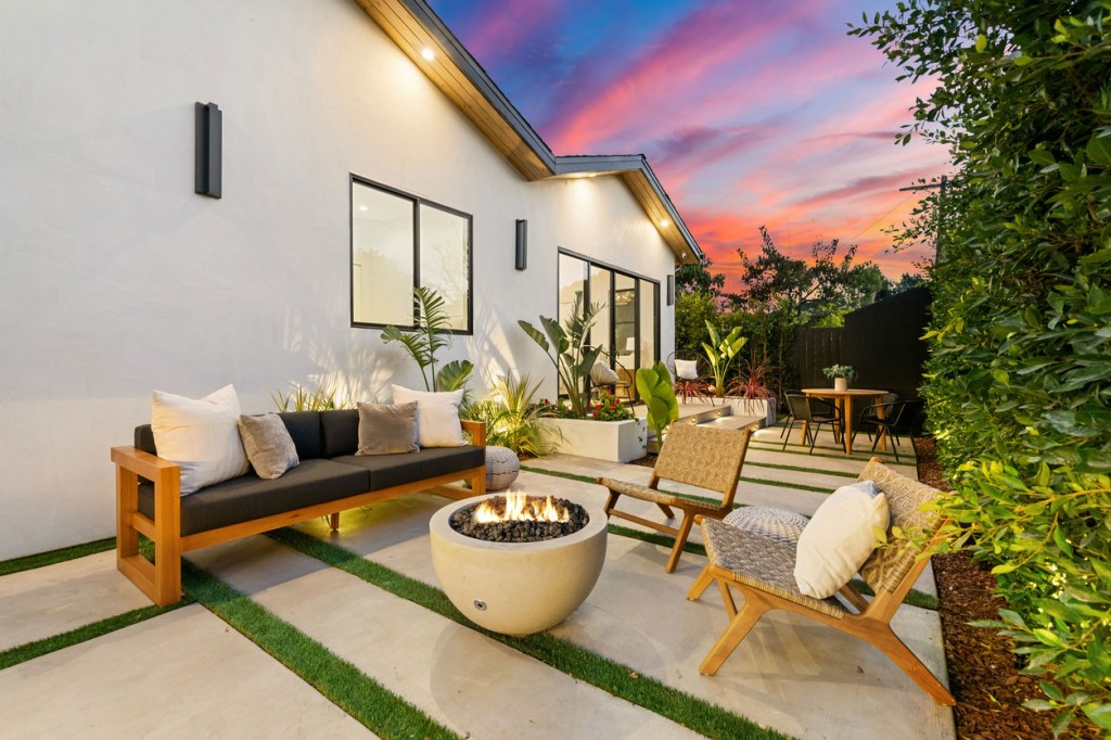 Modern outdoor patio with cozy seating and fire pit, set against a vibrant sunset sky, showcasing contemporary design and lush greenery.